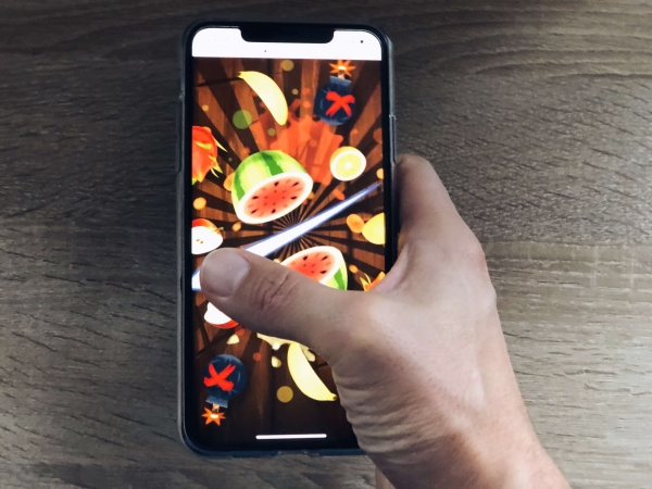 Prst na dotykovom displeji smartfónu pri hre Fruit Ninja
