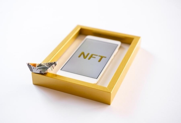 Papierová lodička z bankovky položená na zlatom ráme s telefónom a nápisom NFT